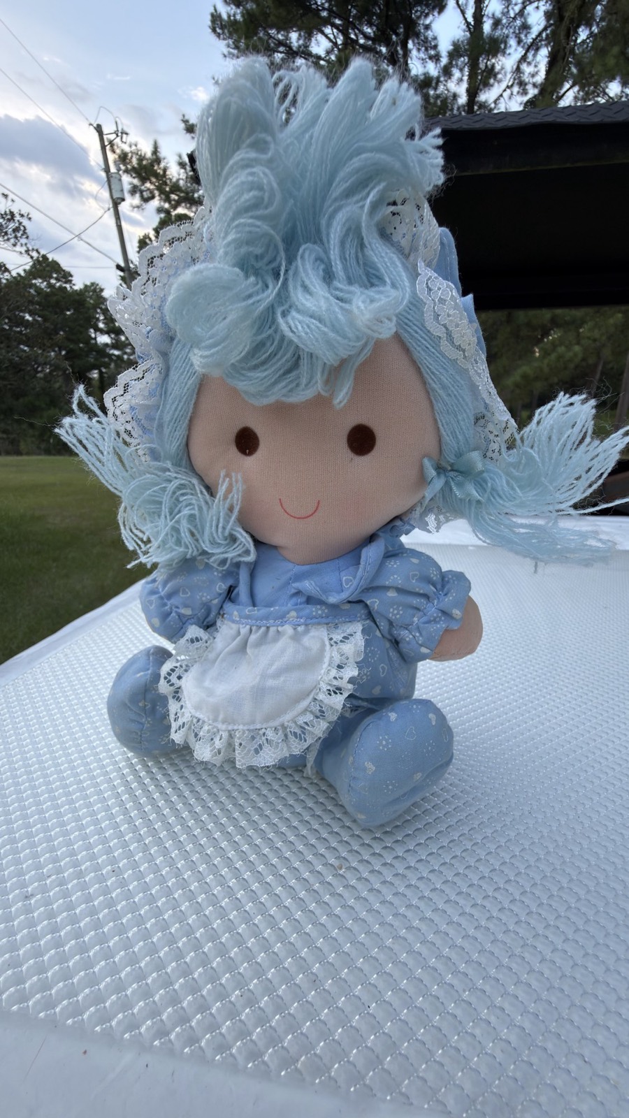 Dan Dee blue rag doll seated outdoors, front view showing the powder-blue yarn topknot and fringed pigtails