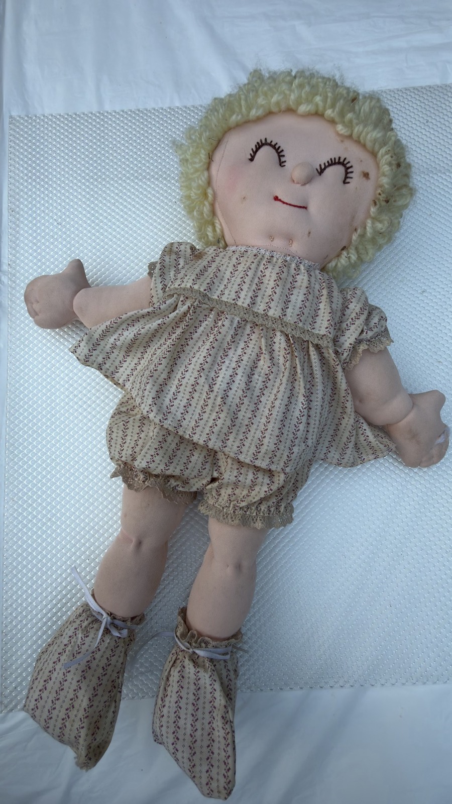 Soft-sculpture baby doll at an angle, showing the cream sprig-print pinafore and lace-trimmed ruffled bloomers