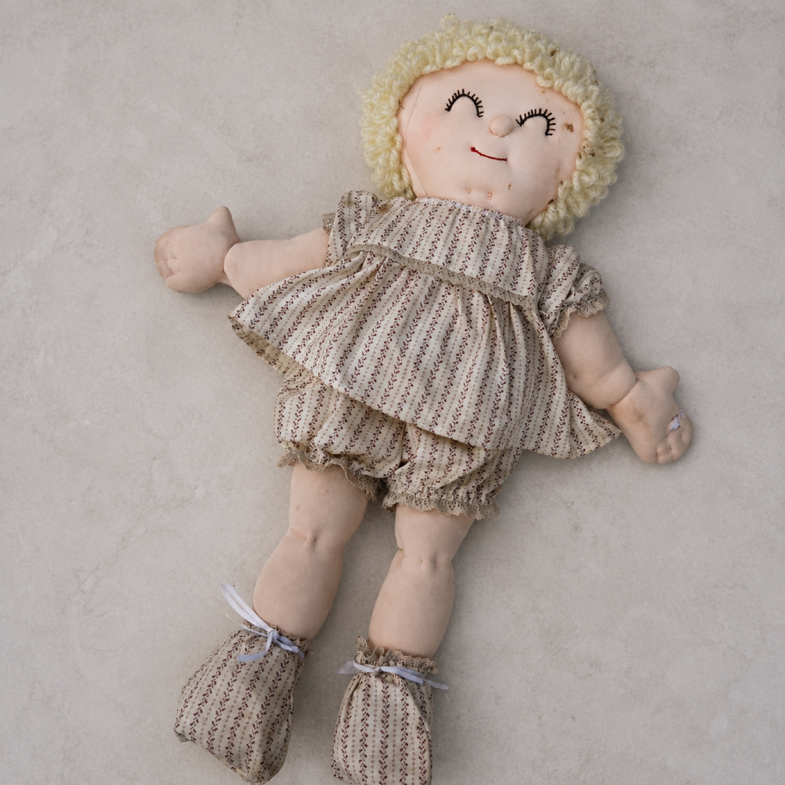 Handmade soft-sculpture baby doll, full front view — needle-sculpted sleeping face with pale yellow loop-curl yarn hair