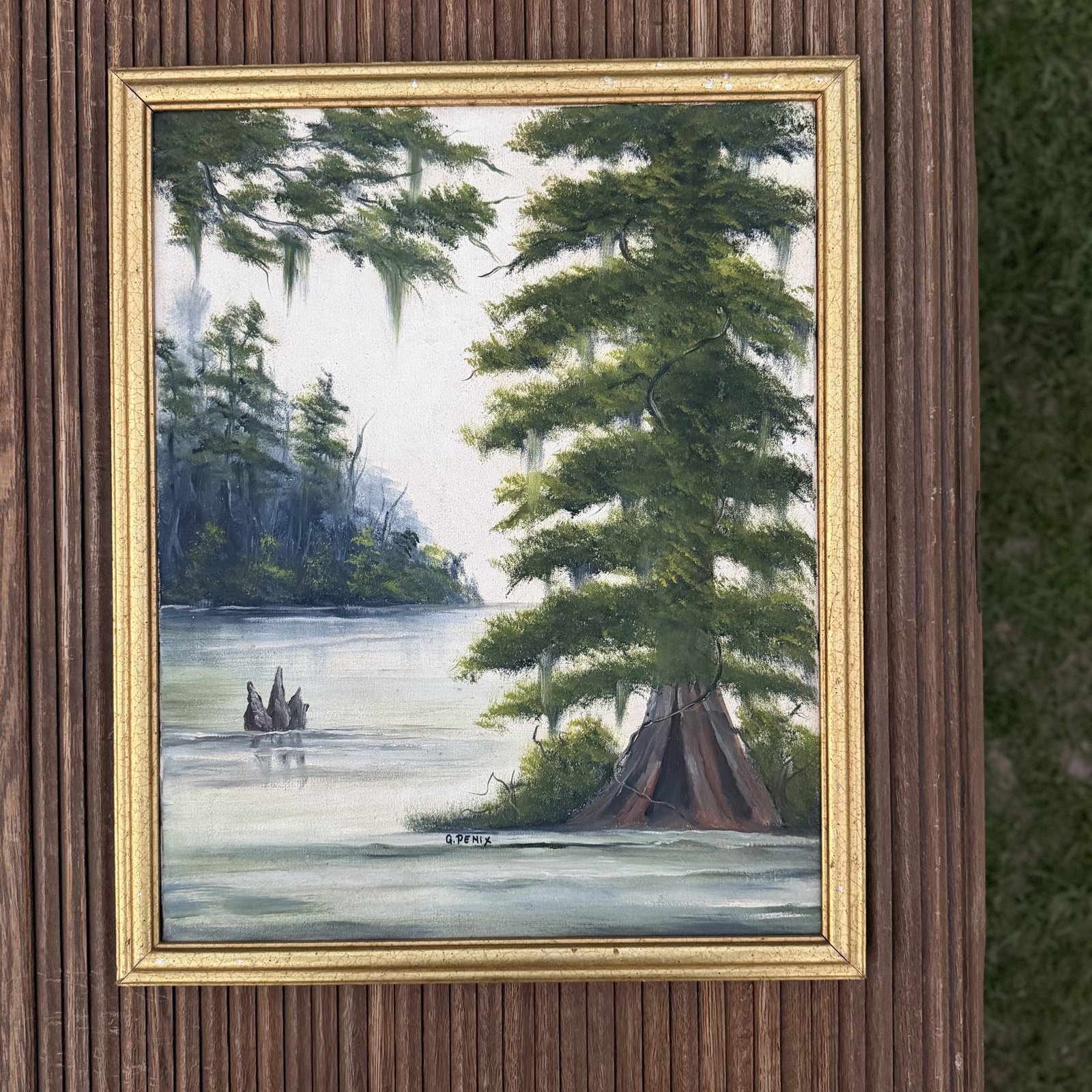 The framed cypress swamp oil painting photographed against weathered wood siding