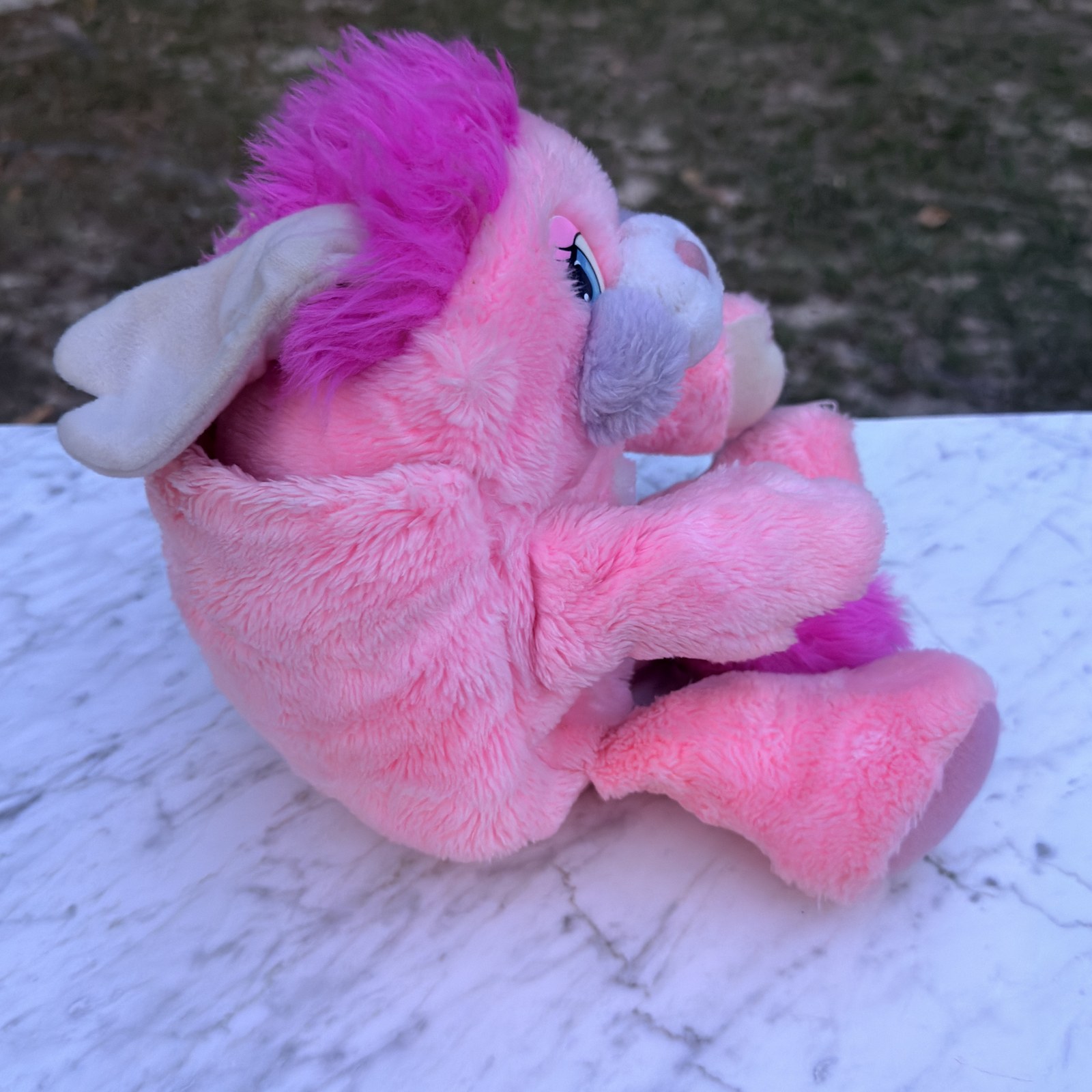 Side view of the Party Popple half-tucked into the pouch, showing the ears and magenta hair