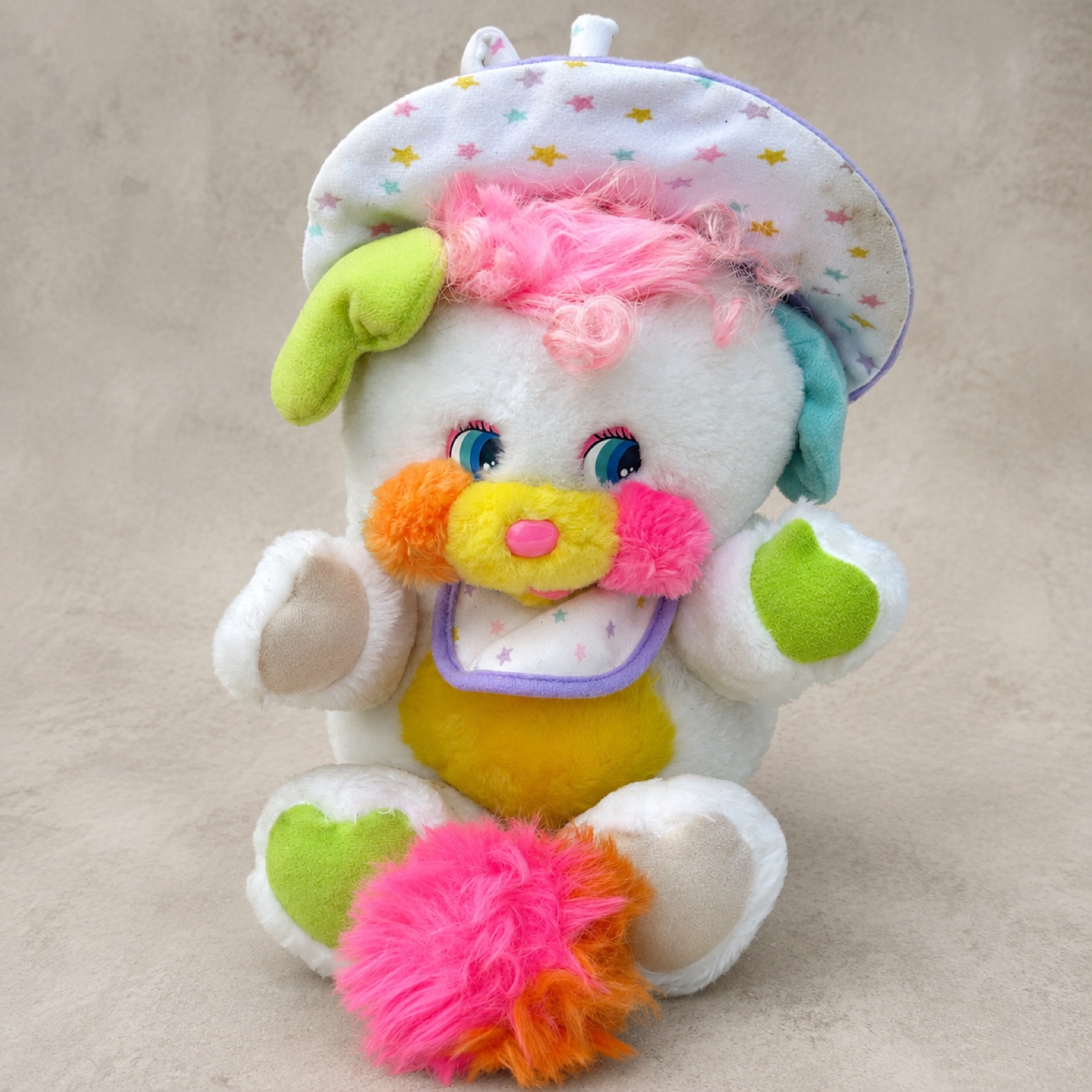 1986 Mattel Baby Cribsy Popple seated front view — white plush with curly pink hair, pastel star-print bonnet and bib