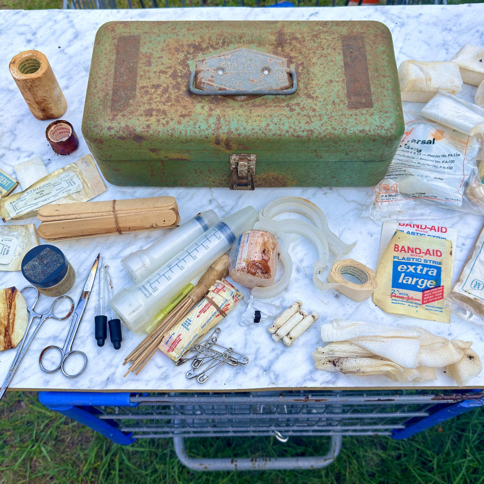 Green steel first-aid case beside its mixed period medical contents