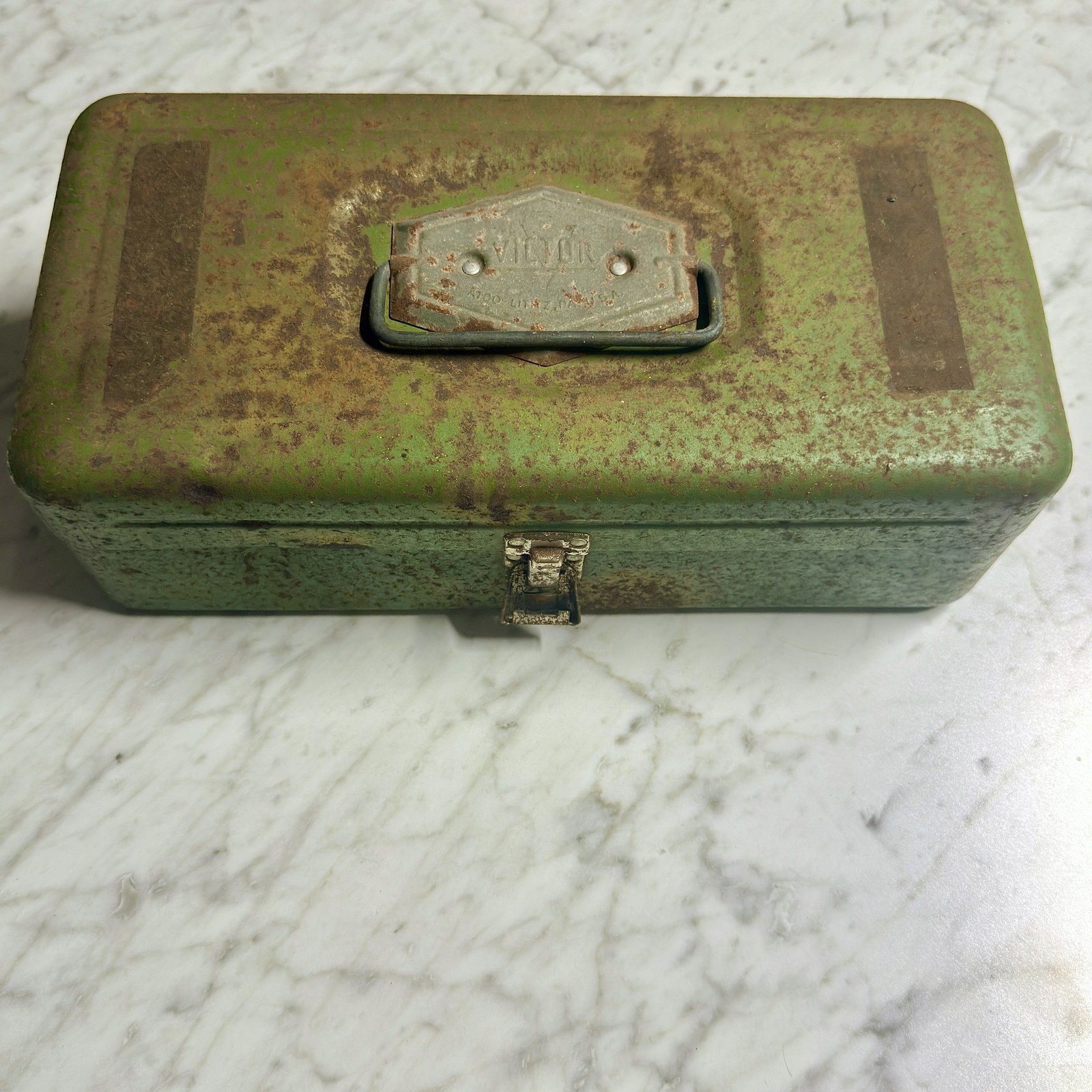 Closed green metal first-aid case, front view, showing honest rust and paint loss